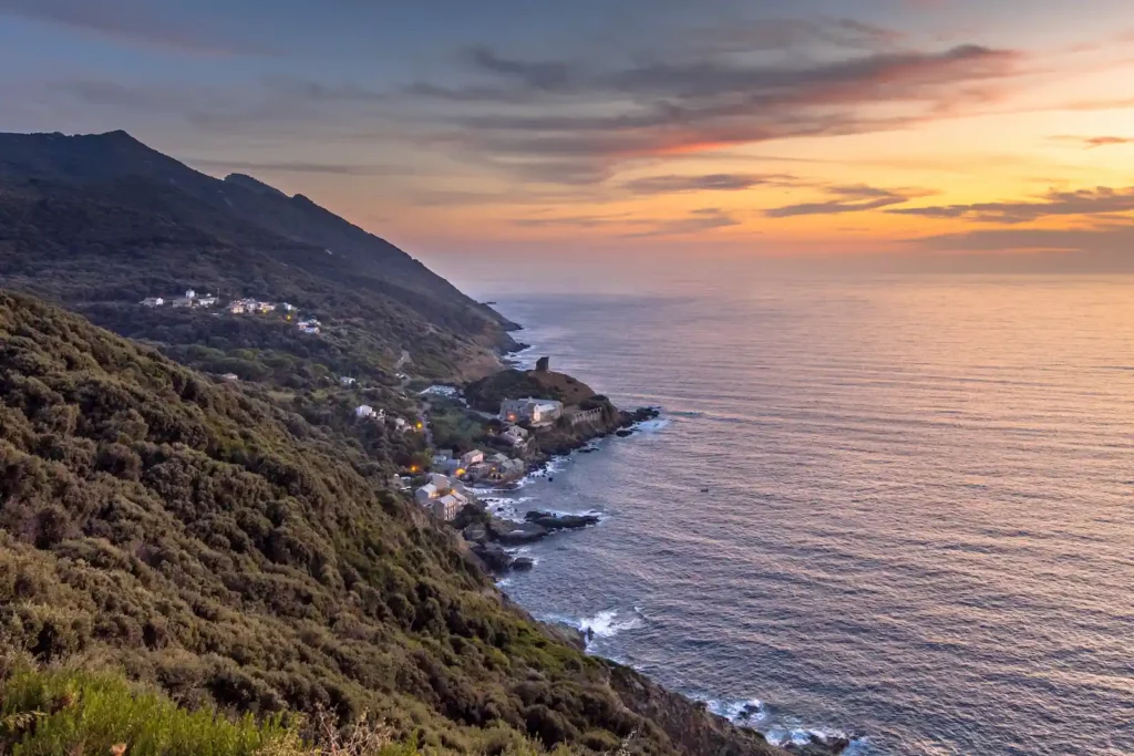 Village Centuri coucher de soleil montagne Littoral corse sauvage au crépuscule, vagues s'écrasant sur les rochers et ciel orangé.