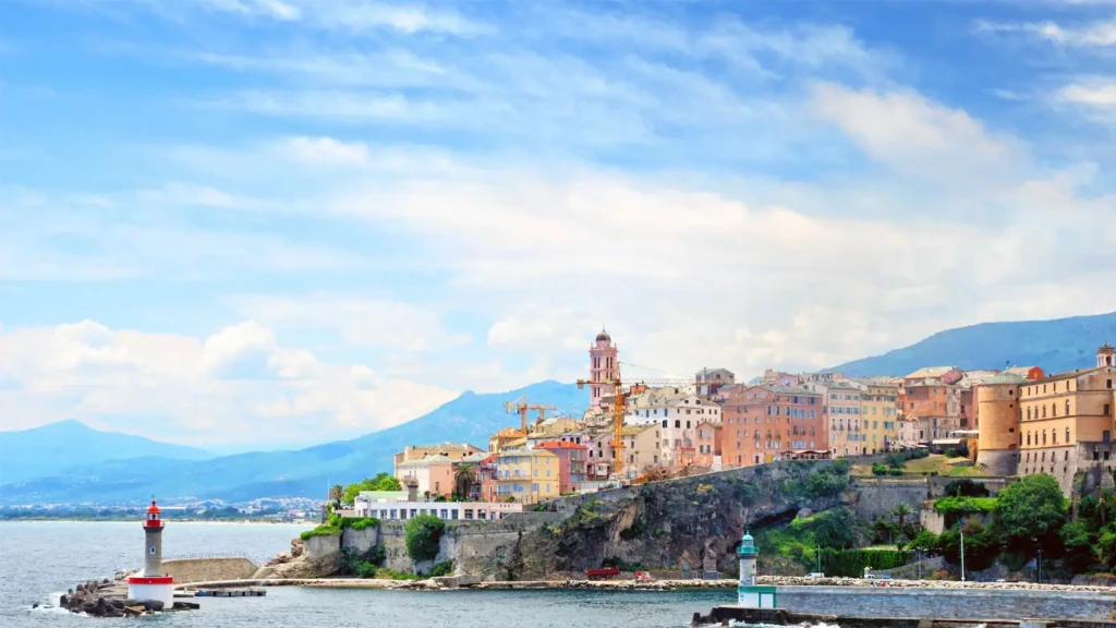 aeroport-bastia-vacances-corse Citadelle historique de Bastia avec ses façades colorées perchée sur une falaise face à la mer Méditerranée et un phare rouge à l'entrée du port.