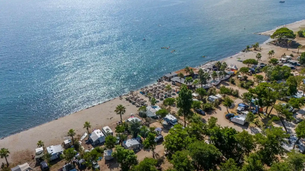 camping-merendella-vue-du-ciel-eau-turquoise-et-azur-avec-plage-de-sable-fin Emplacements ombragés de caravanes et camping-cars au camping Merendella en bord de mer en Haute-Corse avec une plage de sable fin et une mer turquoise sous le soleil.