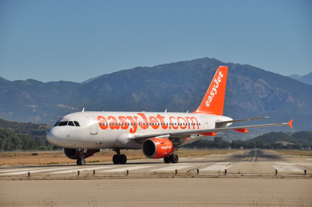 Un avion EasyJet atterrissant à l'aéroport d'Ajaccio en Corse, avec un horizon montagneux sous un ciel ensoleillé.