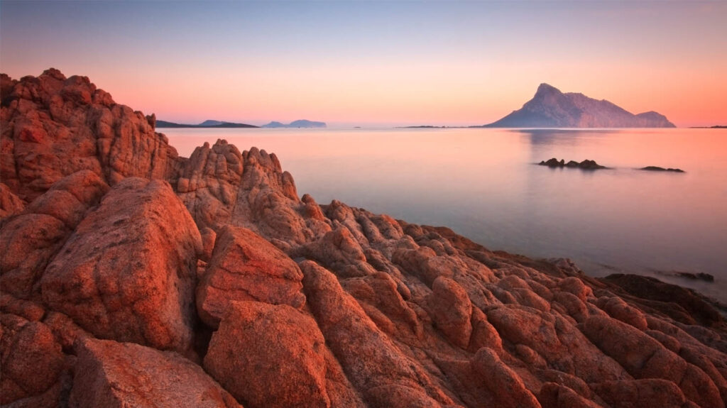 Coucher de soleil enchanteur sur la côte corse, illuminant les rochers escarpés sous des teintes roses et dorées.
