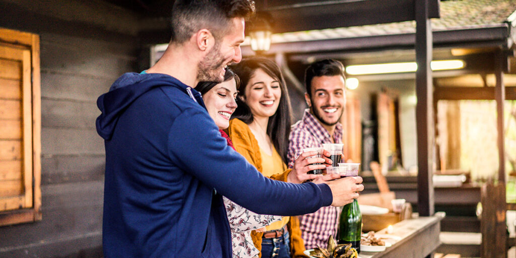 Cinq amis partagent un moment joyeux en levant leurs verres dans un décor en bois à l'ambiance chaleureuse et montagnarde.