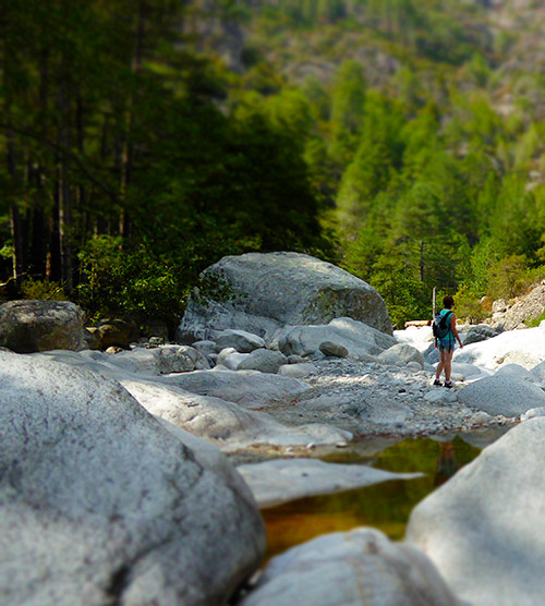 Personne contemplant une rivière tranquille, entourée de roches et de végétation luxuriante dans une vallée paisible.