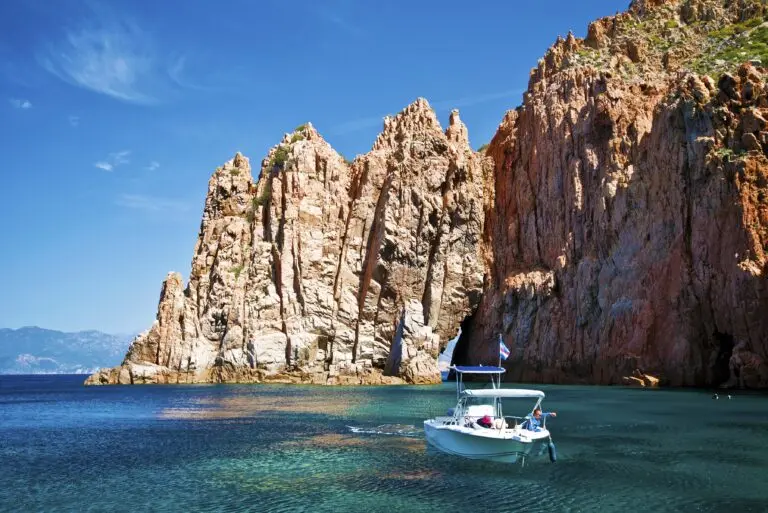 Bateau au large des calanques de Piana en Corse, naviguant sur une mer turquoise sous le ciel ensoleillé. Paysage impressionnant de formations rocheuses, symbole de la nature sauvage corse.