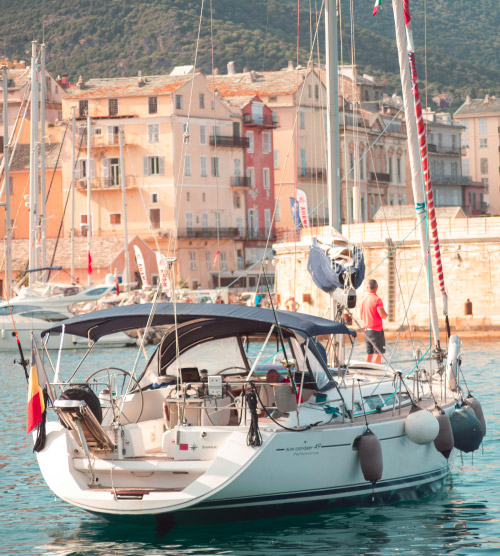 Dans le port animé de Bastia, un élégant bateau à voile se dresse majestueusement, évoquant des vacances méditerranéennes paradisiaques.