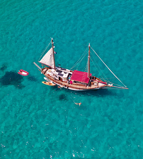Un voilier traditionnel glissant sur une mer bleue éclatante avec des vagues ensoleillées, symbolisant le rêve marin et l'artisanat traditionnel.