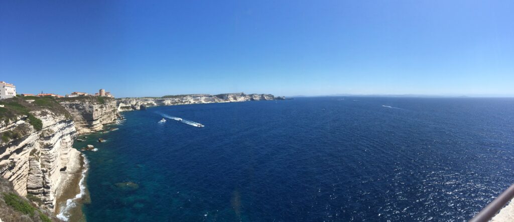 Vue spectaculaire des falaises blanches de Bonifacio surplombant la mer cristalline sous un ciel bleu éclatant.