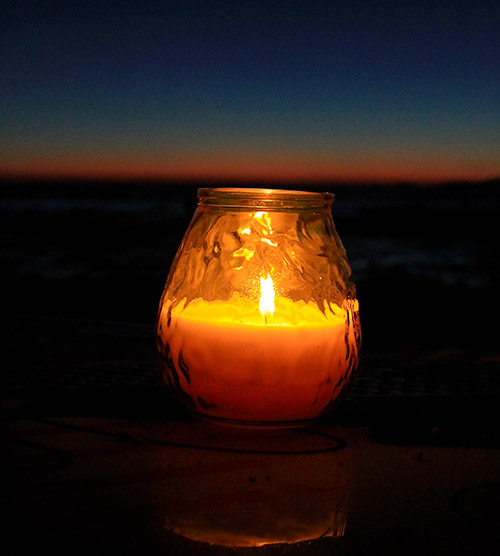 Image d'une bougie scintillante sur une table, éclairant une plage au coucher du soleil, ambiance chaleureuse et apaisante.
