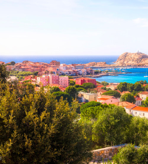 Vue aérienne de l'Île Rousse : mer turquoise, falaises majestueuses, maisons colorées, ciel bleu.