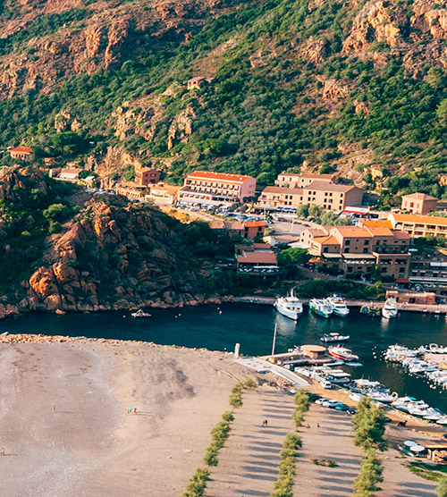 Port de Porto en Corse, révélant ses paysages authentiques et sereins avec bâtiments rustiques, mer scintillante et bateaux amarrés.