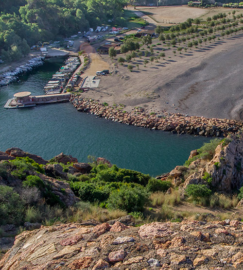 Vue aérienne d'un port de plaisance avec des bateaux et une plage entourée de nature verdoyante, idéale pour la détente et les vacances.