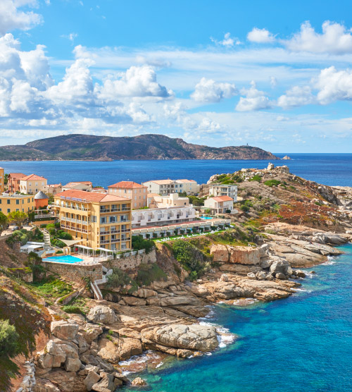 Vue exceptionnelle sur la mer turquoise de Calvi, entourée de falaises majestueuses et de bâtiments colorés sous un ciel méditerranéen lumineux.