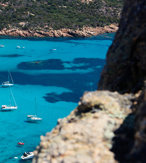 Cette image montre des bateaux naviguant sur une mer turquoise entourée de rochers et végétation, typique de la Corse.