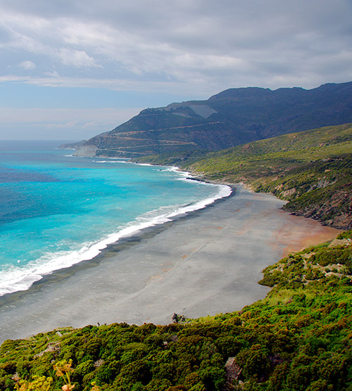 Vue spectaculaire d'une côte sauvage où l'océan bleu turquoise rencontre des collines verdoyantes et des montagnes imposantes; l'image captive par sa tranquillité et son harmonie naturelle.