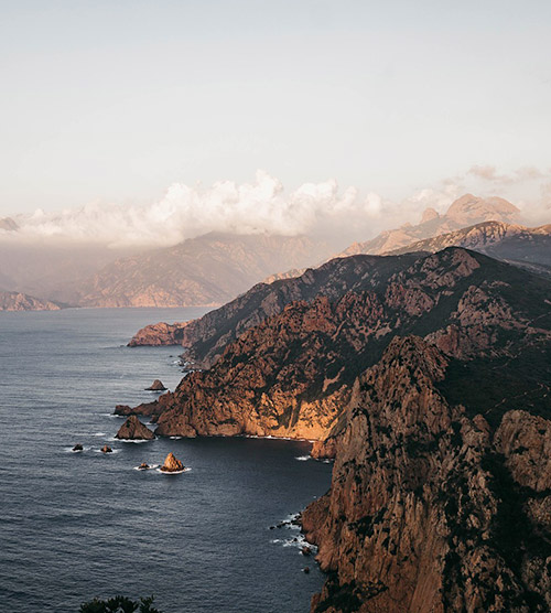 Scène sereine du littoral où les montagnes rejoignent la mer sous un ciel teinté de doré au crépuscule