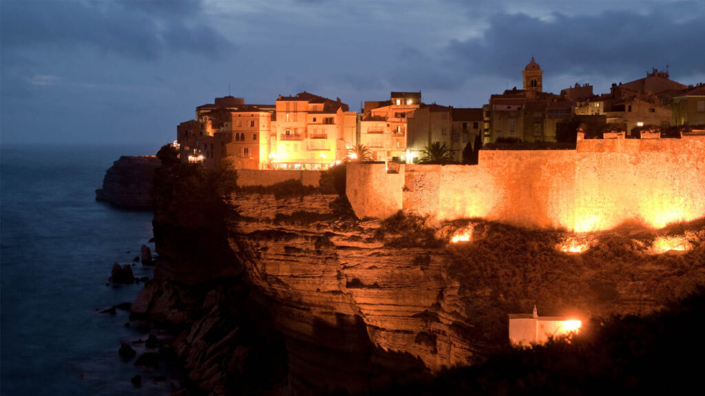 Village corse majestueusement éclairé au coucher du soleil, offrant un panorama sur la mer avec bâtiments historiques en pierre.