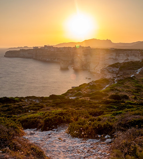 Vue spectaculaire des falaises de Bonifacio illuminées par un coucher de soleil doré, mêlant couleurs chatoyantes et tranquillité méditerranéenne, pour un moment de paix et d'émerveillement.