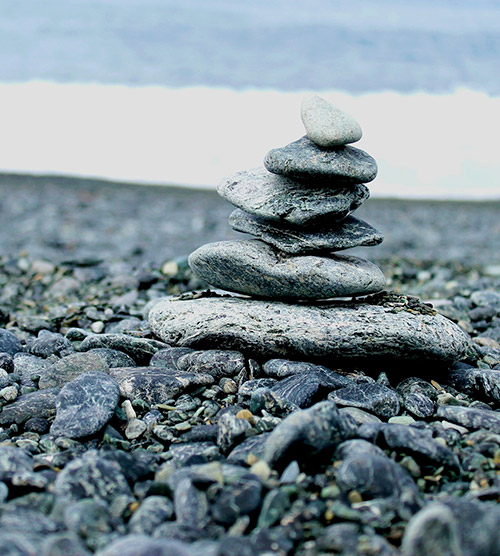 Empilement de pierres grises soigneusement équilibrées sur une plage tranquille, évoquant sérénité et méditation dans un cadre naturel apaisant.