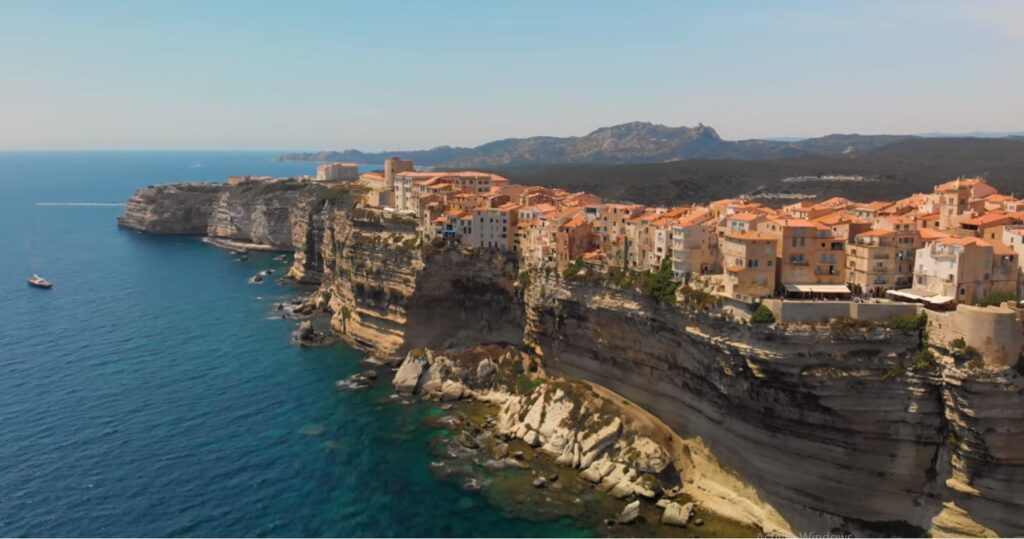 Vue des spectaculaires falaises de Bonifacio en Corse, avec des maisons colorées ancrées dans la roche surplombant une mer Méditerranée éclatante.