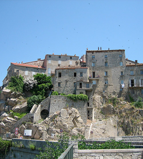 Cette image montre les maisons en pierre caractéristiques de Sartène, regroupées sur un rocher, sous un ciel bleu éclatant en Corse.