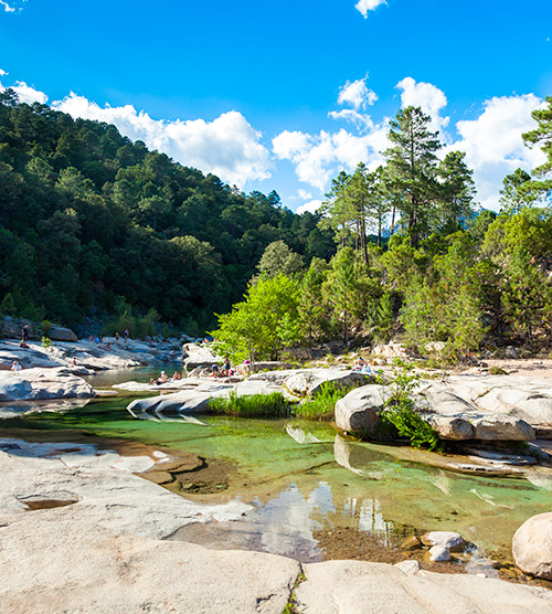 Image d'une rivière paisible entourée de montagnes verdoyantes sous un ciel bleu avec des reflets d'eau cristalline, idéale pour une évasion sereine en pleine nature.
