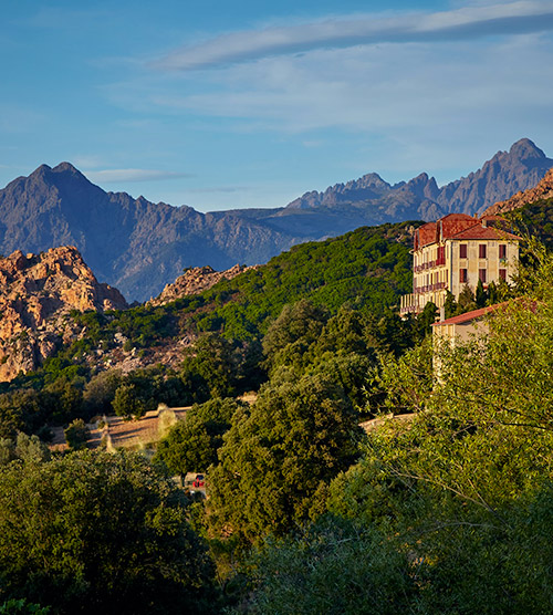 Paysage pittoresque d'un village corse niché dans une vallée verdoyante, avec montagnes environnantes et lumières du soleil.