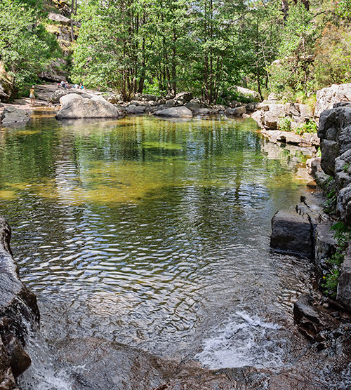 Image d'une piscine naturelle sereine entourée de rochers et de végétation luxuriante avec des personnes se relaxant, idéale pour échapper au quotidien.