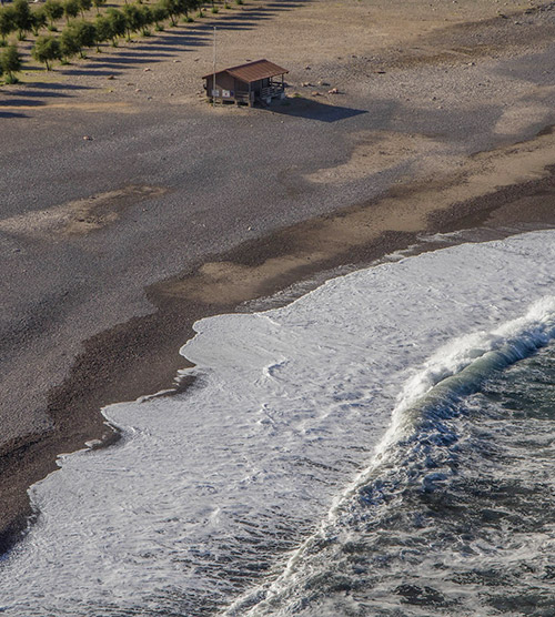 Petite maison en bois sur une plage paisible avec vagues et lumière du soleil créant une atmosphère apaisante.