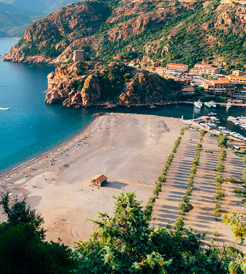 Vue magnifique d'une plage dorée en Corse avec un village méditerranéen en arrière-plan, parfait pour des vacances relaxantes.