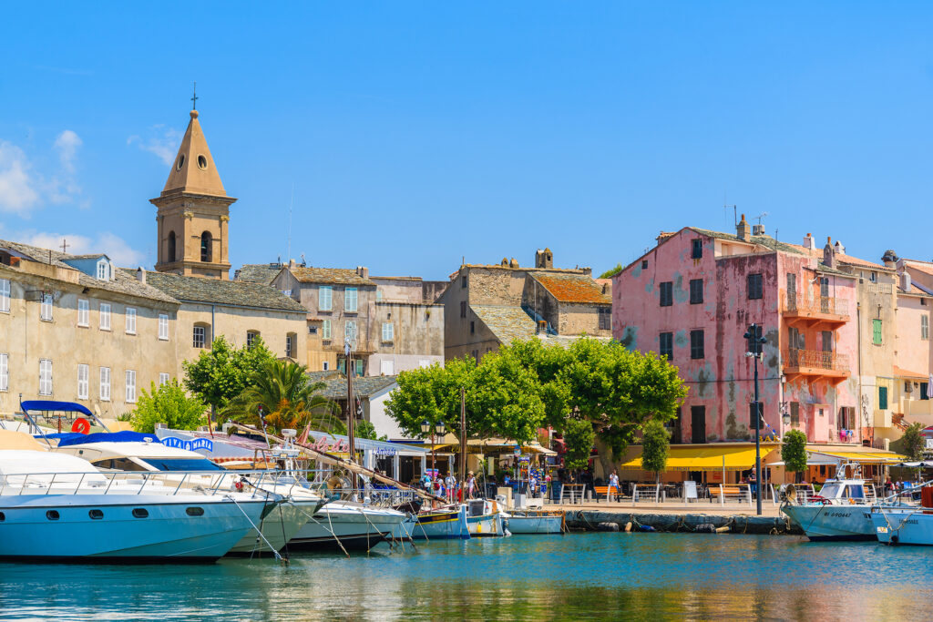 Port pittoresque de Saint-Florent illustrant des yachts élégants devant des maisons pastel méditerranéennes, baigné par la lumière du matin et l'atmosphère paisible de la Corse.