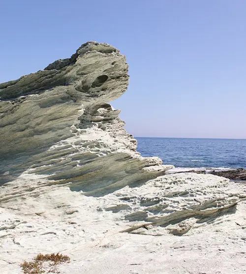 Paysage côtier captivant avec un rocher marin sculpté par le temps, entouré de vagues et éclairé par un ciel azur.