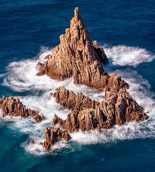 Dans les profondeurs de l'océan, un groupe de rochers puissants émerge sous un ciel bleu, entouré de vagues dynamiques et éclaboussantes.