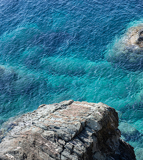 Une mer bleue éclatante vue depuis un rocher, avec des nuances turquoise et des reflets lumineux, invitant à la méditation.