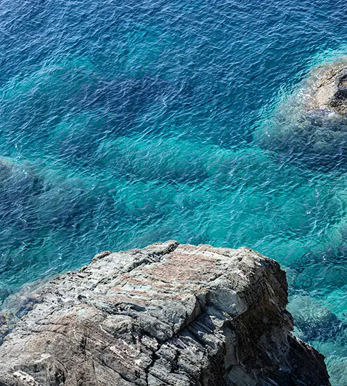 Une mer bleue éclatante vue depuis un rocher, avec des nuances turquoise et des reflets lumineux, invitant à la méditation.