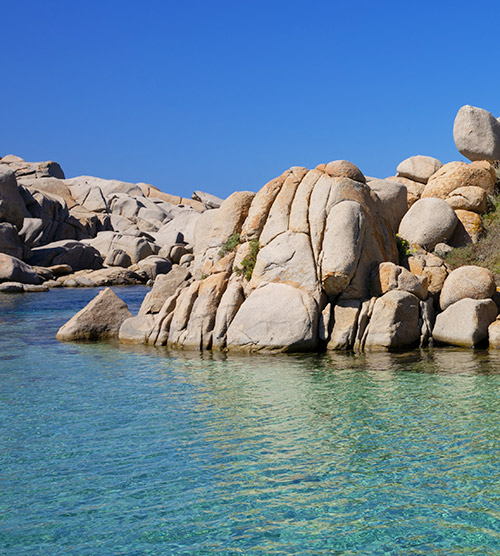 Image de rochers émergeant d'une mer cristalline et paisible, illuminée par la lumière du soleil, offrant une scène idéale pour la contemplation et la rêverie.