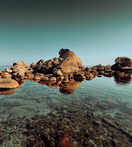 Cette image montre un cadre naturel avec des rochers émergeant d'une eau limpide sous un ciel bleu, exprimant calme et tranquillité en pleine harmonie maritime.