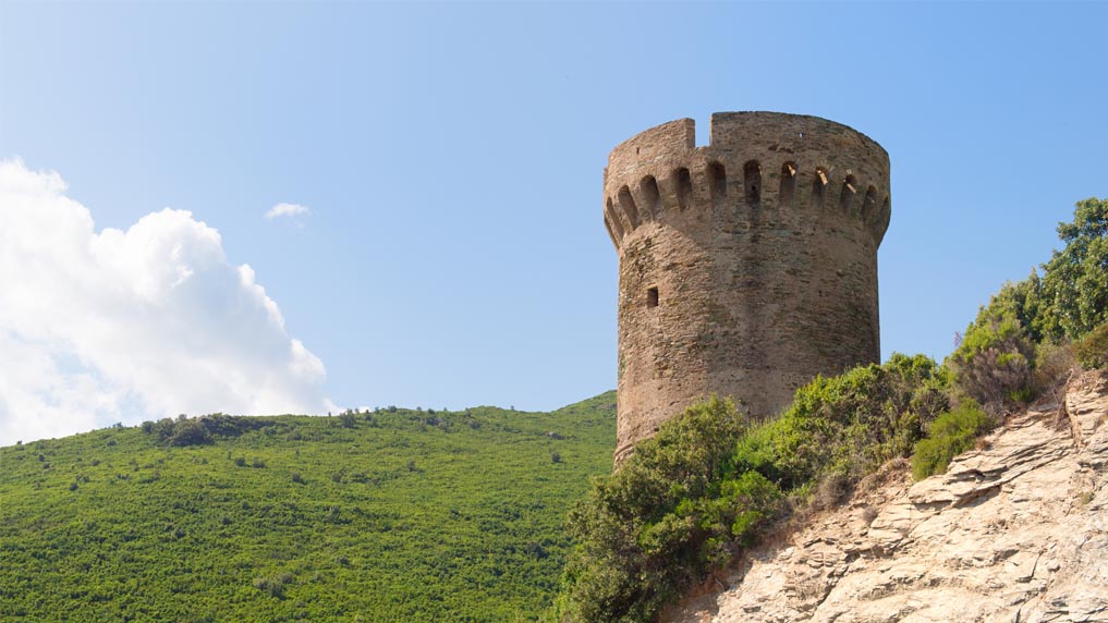 Tour en pierre nichée sur une colline verdoyante sous un ciel bleu, offrant une vue panoramique et témoignant de l'harmonie entre l'homme et la nature.