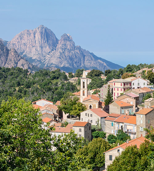 Photo captivante montrant un village corse pittoresque baigné de soleil, entouré de montagnes, capturant une atmosphère sereine et naturelle idéale pour des vacances inoubliables.