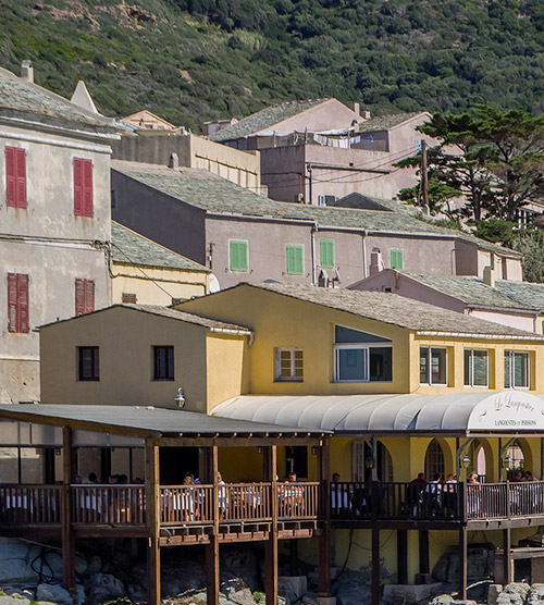 Charmant village côtier en Corse avec des maisons colorées, entourées de montagnes majestueuses et une mer scintillante.