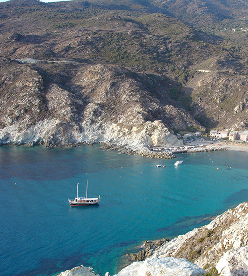 Paysage côtier en Corse avec un bateau sur des eaux cristallines, entouré de montagnes et de plages sablonneuses.