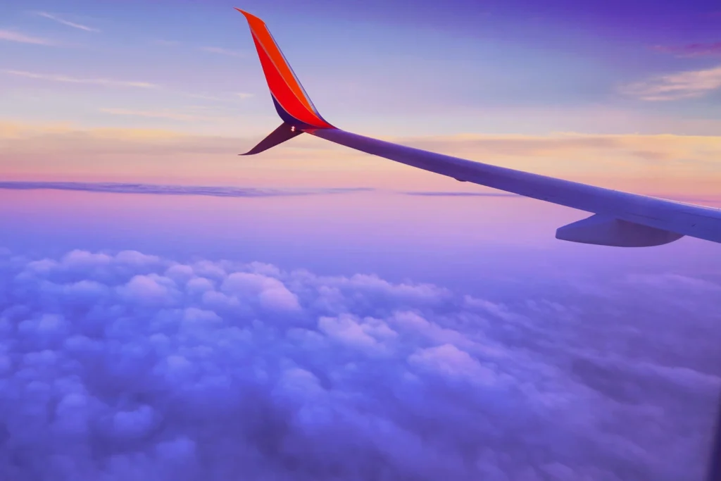 vue_avion_nuages_coucher_soleil_ciel_paisible Vue aérienne impressionnante d'un avion survolant des nuages colorés par le coucher de soleil, reflétant une sérénité magique.