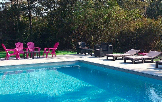 Dans un cadre naturel apaisant, une piscine scintillante entourée de transats et de sièges colorés invite à la détente en famille ou entre amis sous un ciel bleu.