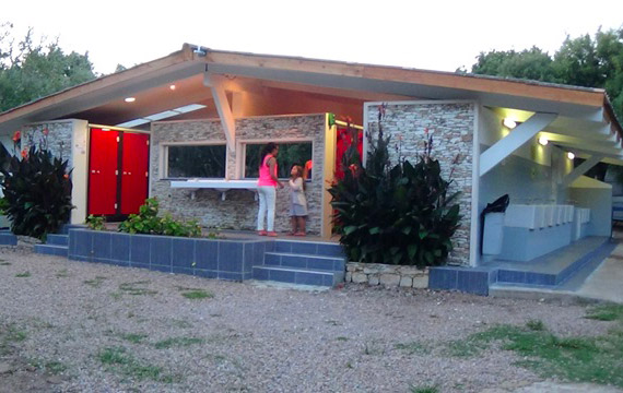 Centre de services convivial et moderne au camping Cavallo Morto à Bonifacio, entouré de plantes tropicales et au design dynamique, parfait pour des rassemblements familiaux.