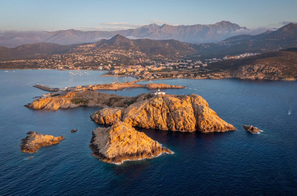 Paysage de crépuscule corse avec montagnes et mer, capturant l'harmonie entre nature et architecture.