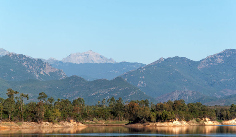 Le paysage captivant montre des montagnes majestueuses se reflétant dans un lac paisible sous un ciel bleu, entouré de forêts verdoyantes, créant une ambiance sereine et esthétiquement harmonieuse.