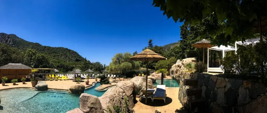 Questa immagine evoca evasione e relax a bordo piscina in Corsica, un luogo perfetto per ricaricarsi, con la sua atmosfera tranquilla, la cornice naturale e il calore accogliente. Una vera oasi di pace.