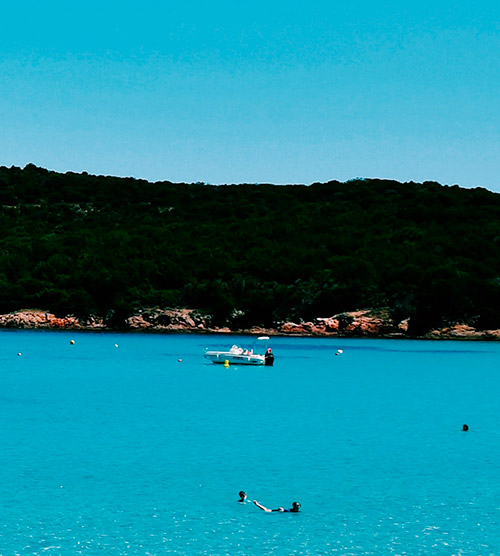 Au cœur d'une mer turquoise, des baigneurs profitent du soleil et d'un bateau glissant sur les vagues, offrant une illustration parfaite de la détente estivale sur une plage.