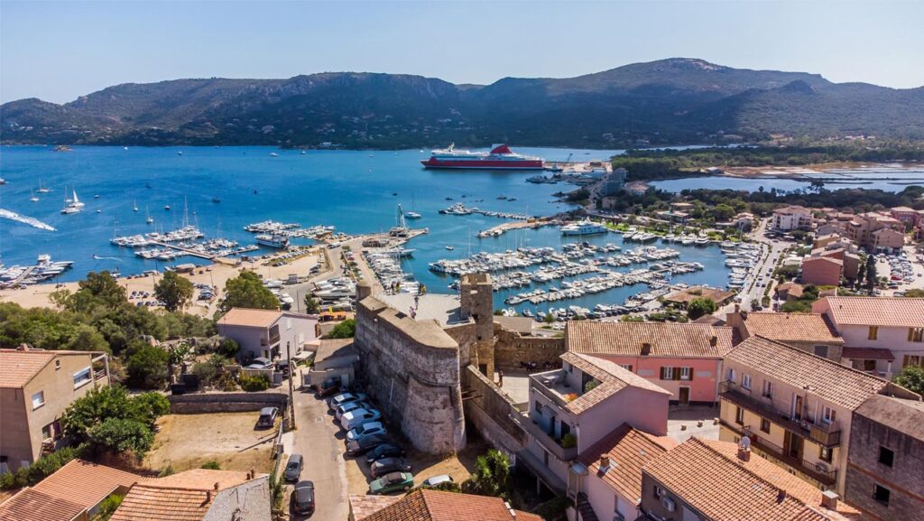 Cette vue aérienne de Porto-Vecchio capture la marina pleine de bateaux avec les collines corses en arrière-plan, transmettant une ambiance sereine et ensoleillée.