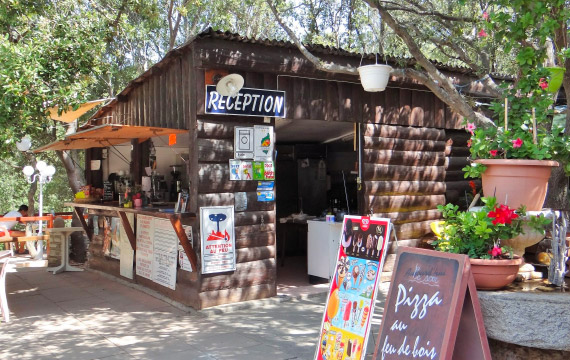 Une cabane de réception accueillante et naturellement décorée au camping Stella Patrimonio, offrant un lieu charmant près de la mer où les vacanciers peuvent se renseigner et déguster des pizzas au feu de bois.