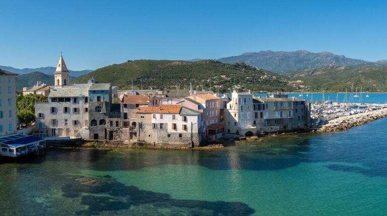 Village en Corse avec maisons colorées, mer et bateaux, reflétant la tranquillité et le charme méditerranéen.